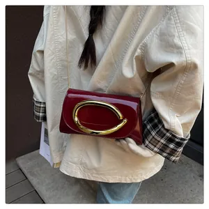 Close-up of luxury burgundy patent leather crossbody bag with bold golden buckle detail