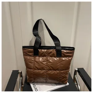 Detail of dark brown quilted puffer tote bag with glossy finish on a leather chair