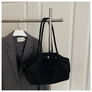 Detail of black suede tote bag with metal buckles hanging on a rack in a minimalist setting