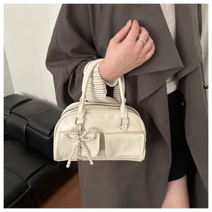 Close-up of cream leather Boston bag with pearl bow charm and stylish front pockets
