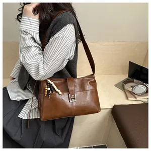 Detail of retro brown leather shoulder bag featuring a beaded tassel and square buckle