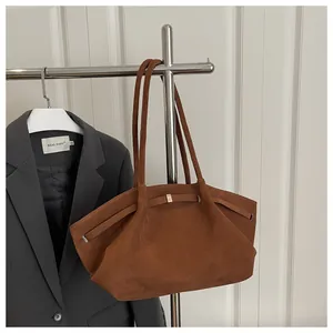 Detail of a brown suede bucket bag featuring a sleek metal buckle and long shoulder strap