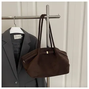 Detail of a dark brown suede bucket bag with a gold buckle hanging on a metal stand