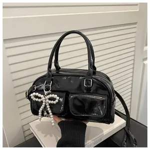 Detail of black patent leather Boston bag with front pockets and pearl bow charm