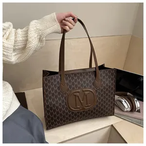Close-up of brown tote bag with M-letter prints and embossed logo in a lifestyle setting