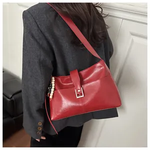 Red leather shoulder bag shown on model with silver buckle and beaded pendant detail