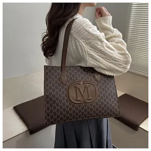 Close-up of large tote bag with M-letter pattern and leather logo on a shoulder strap