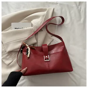 Detail of burgundy shoulder bag with silver buckle and decorative beaded tassel pendant