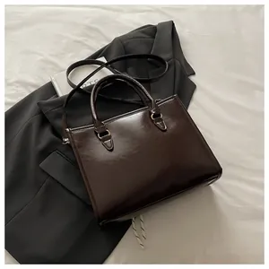Detail of a dark brown glossy leather tote bag with elegant golden hardware and handle