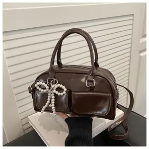 Detail showing deep brown glossy Boston bag with pearl bow charm and top handle