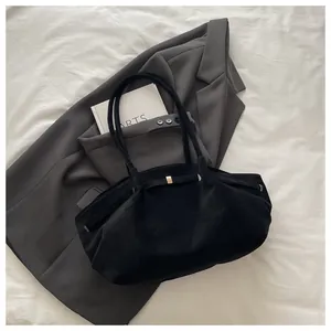 Close-up of black matte bucket bag with gold bow ornament on grey blazer background