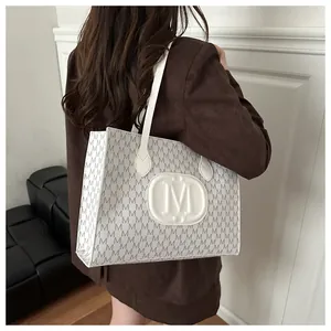 Detail of white tote bag with M-letter monogram pattern and embossed oval logo