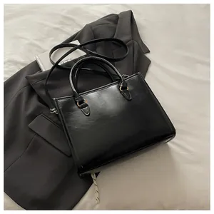 Detail view of black rectangular tote with gold hardware on grey suit background