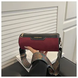 Detail of burgundy suede cylinder bag with black leather trim and ethnic woven strap
