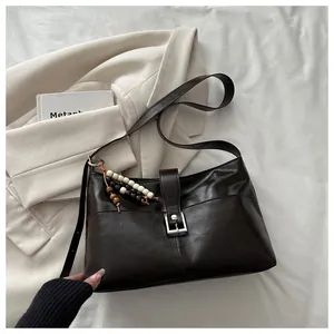 Close-up of dark brown vintage faux leather shoulder bag with beaded charm and silver buckle