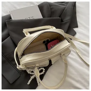 Detail showing the spacious interior of a cream white Boston bag with a pearl bow charm
