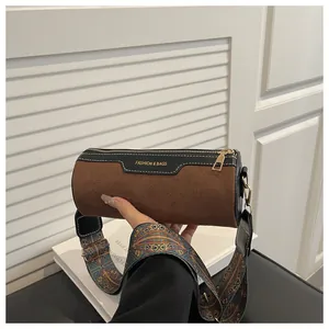 Detail of cylinder crossbody bag featuring brown suede and black leather patchwork design