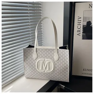 Detail of a chic cream tote bag featuring embossed M patterns and a stylish shoulder strap