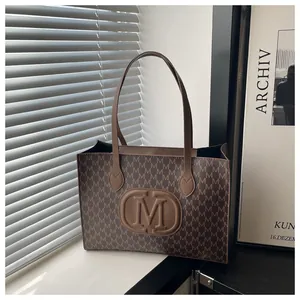 Detail view of brown tote bag featuring vintage M-letter prints and embossed logo