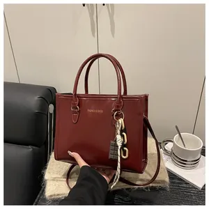 Detail of burgundy leather tote featuring gold fashion logo and chocolate chain charm