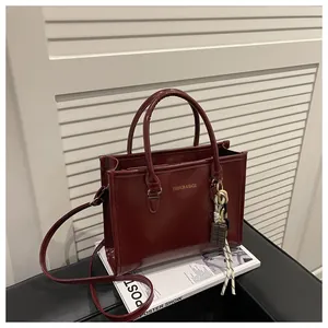 Detail of burgundy glossy leather handbag with fashion charm and golden logo lettering
