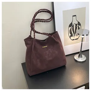 Details der gewebten Griffe und des Markenlogos an der burgunderroten Wildledertasche