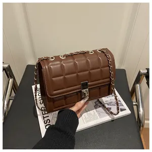 Detail of brown quilted square bag featuring silver chain strap and metal clasp on magazines