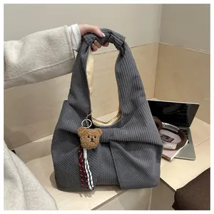 Détail d'un sac à main en velours côtelé gris foncé avec nœud géant et breloque ours