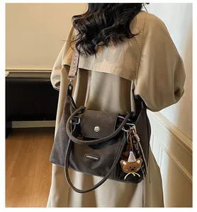 Detail of dark brown matte leather handbag with wide geometric strap and cute bear charm