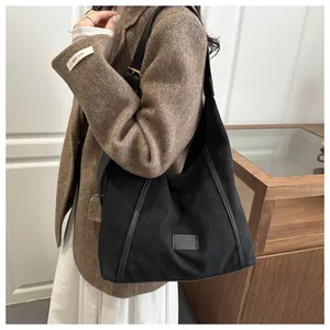 Side view of a black canvas tote bag with leather straps on a model wearing a brown blazer