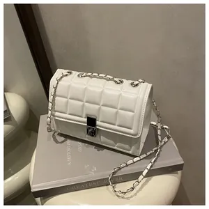 Detailed shot of white quilted square bag with silver chain strap on a minimalist book