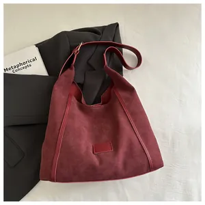 Close-up of a burgundy hobo bag in suede and smooth leather on a black blazer backdrop