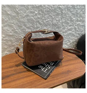 Detail of dark brown suede handbag with gold metal clasp on a black book