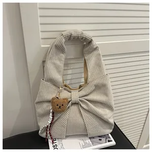 Détail d'un sac à main en velours côtelé blanc cassé avec grand nœud et breloque ours