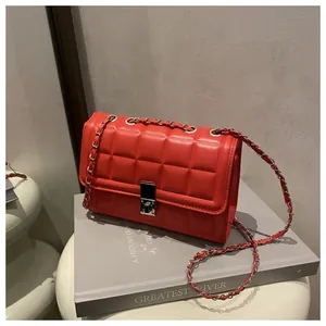 Detailed view of red quilted square bag with silver metal lock and chain strap on book