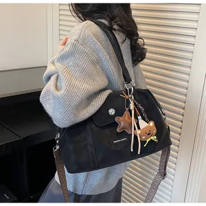 Detail of a black pillow handbag with wide woven strap and cute bear pendant charms