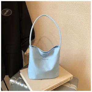 Detalle del bolso tipo cubo azul claro con bordado sobre una maleta plateada