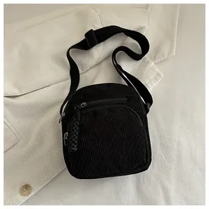 Détail de la texture en velours côtelé noir et des poches zippées du sac bandoulière épuré