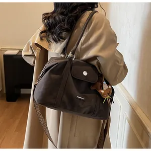 Brown canvas tote bag with wide strap and teddy bear charm shown on a model's shoulder