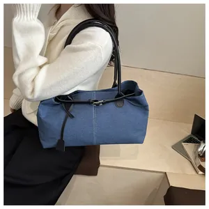 Detail of blue denim tote bag featuring black leather handles and metal buckle closure