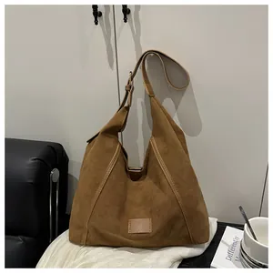 Close-up of brown suede crossbody bag with adjustable strap on white fabric background