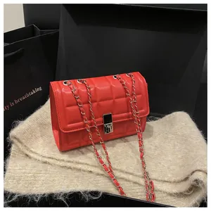 Detailed close-up of a red quilted chain bag with a silver lock on soft beige fabric