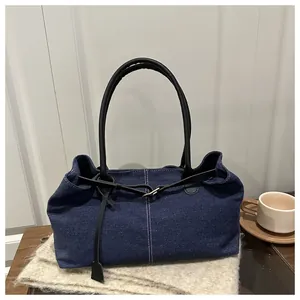 Detailed close-up of dark denim tote bag with leather strap and contrast stitching
