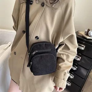 Sac à bandoulière rétro en velours côtelé noir porté par un mannequin dans un décor cosy