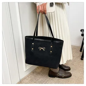 Detail of black suede tote bag with golden bow hardware and long shoulder strap