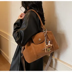 Detail of brown faux suede pillow bag with bear charm and woven wide shoulder strap