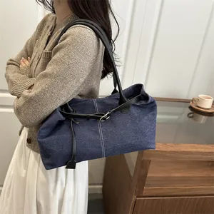 Blue denim tote bag with black leather straps and metal buckle shown on a model
