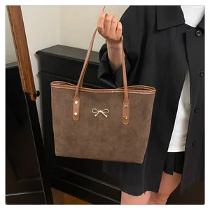 Detail of brown suede tote bag with golden bow ornament and reinforced leather handles