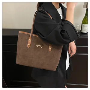 Detail view of coffee-colored suede tote bag with golden bow and leather handles