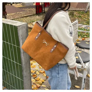 Detail of caramel suede tote bag featuring a gold bow accent and metal studs